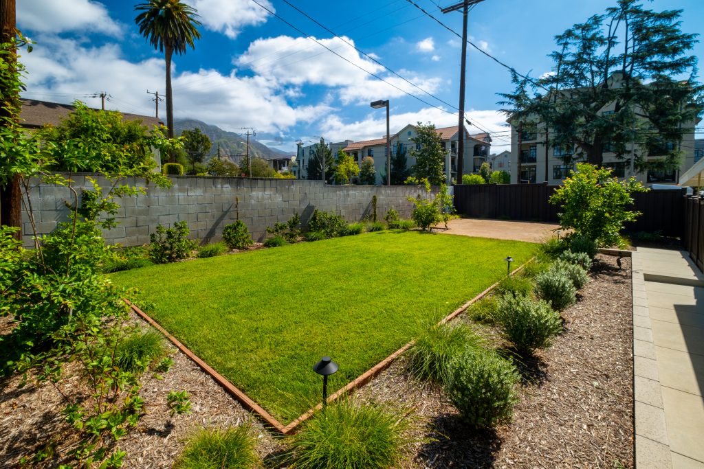 Refreshed backyard lawn bordered by drought-tolerant planting beds, gravel mulch and path lights