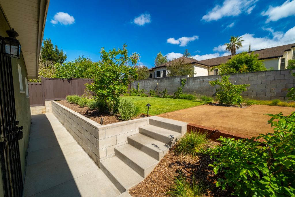 Backyard with a block retaining wall, concrete steps and walkway, and fresh planting beds