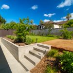 Backyard with a block retaining wall, concrete steps and walkway, and fresh planting beds